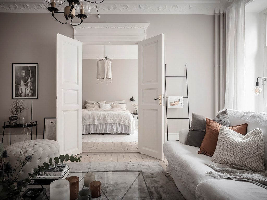A bedroom with greige walls, white bedding, white area rug, wing doors