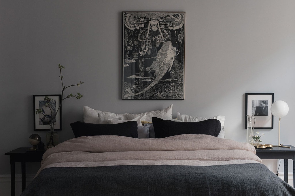 A bedroom with a medium grey wall, black art prints, black throw pillows, black bedside tables