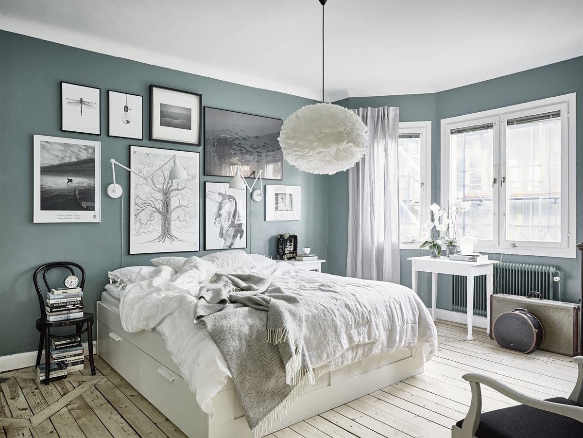 An impressive black and white gallery wall on top of a sage green bedroom wall