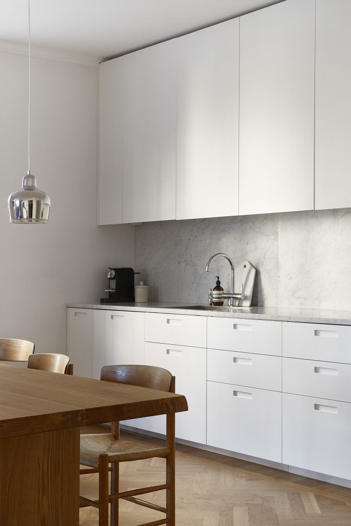 Minimal white kitchen cabinets, Artek golden bell pendant lamps, J39 chars, oak dining table