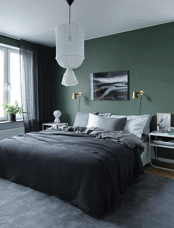 A bedroom with a fresh dark green wall color and gold wall lamps, dark grey textiles