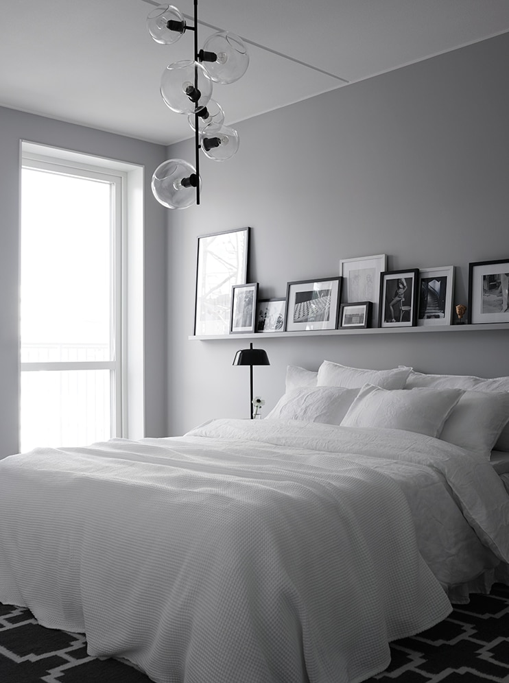 A light grey bedroom with a picture ledge with a mixture of frames and black light fixtures