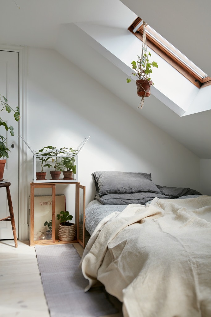 An attic bedroom with white walls and lots of plants