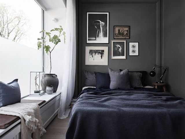 A bedroom with dark grey walls and a black and white gallery wall