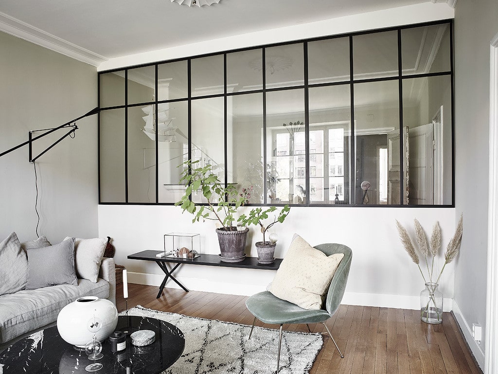 A living room with a glass partition wall letting daylight into the home office