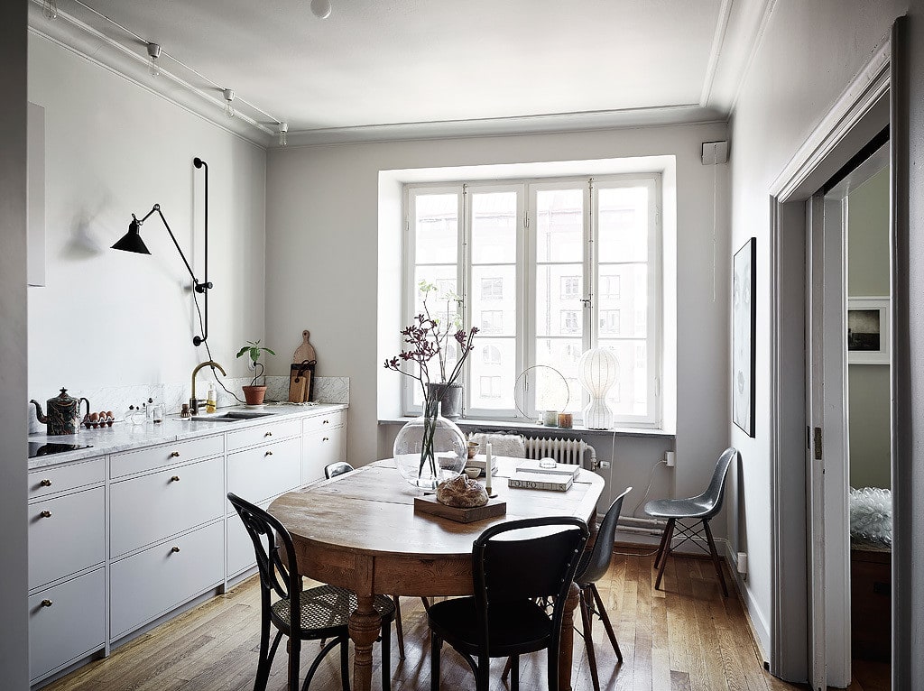 Classy white kitchen, brass faucet, brass cabinet pulls, vintage dining table, black bentwood chairs, black wall lamp, minimal exhaust
