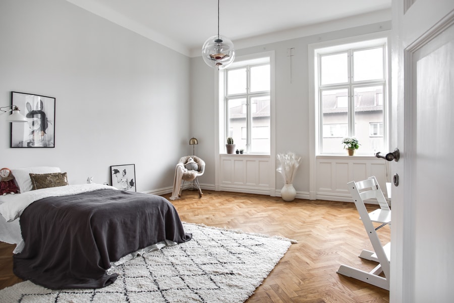 A light grey bedroom with a warm wooden floor and dark grey bedding