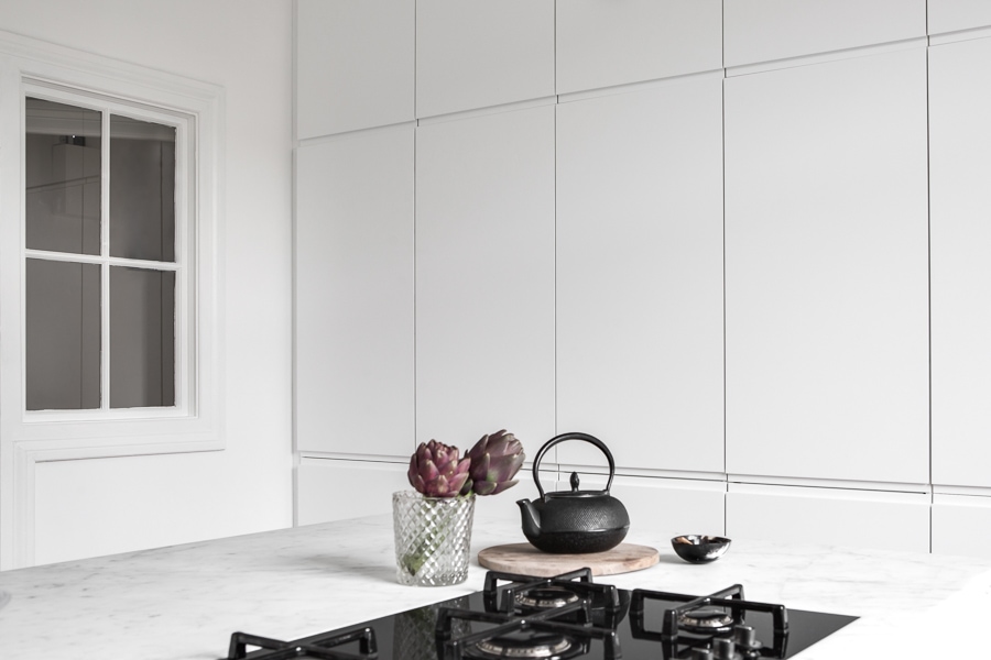 A minimal white kitchen with white marble countertops and a window towards the hallway