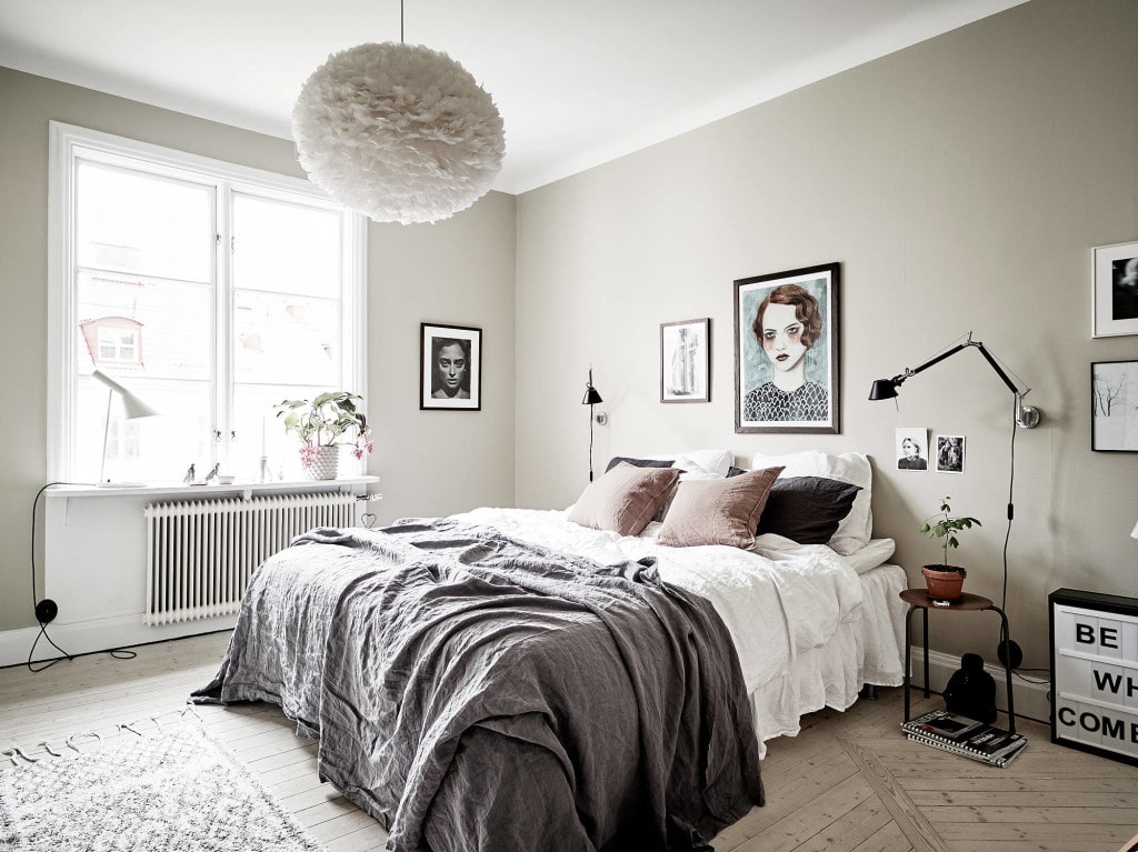 A bedroom with beige walls, a mixture of art prints and pink, white and grey tones in the bedding