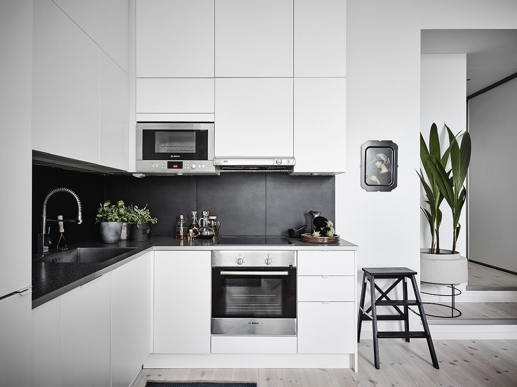 A minimal white kitchen with black countertops, black tile backsplash