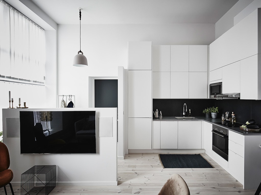 A minimal white kitchen with black countertops, black tile backsplash, TV wall