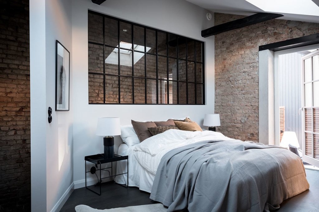 An exposed brick bedroom with a wal and window in front of it