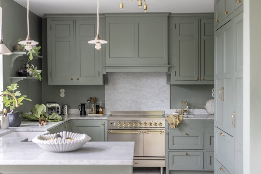 A green shaker kitchen with white marble countertops and gold details in the hardware