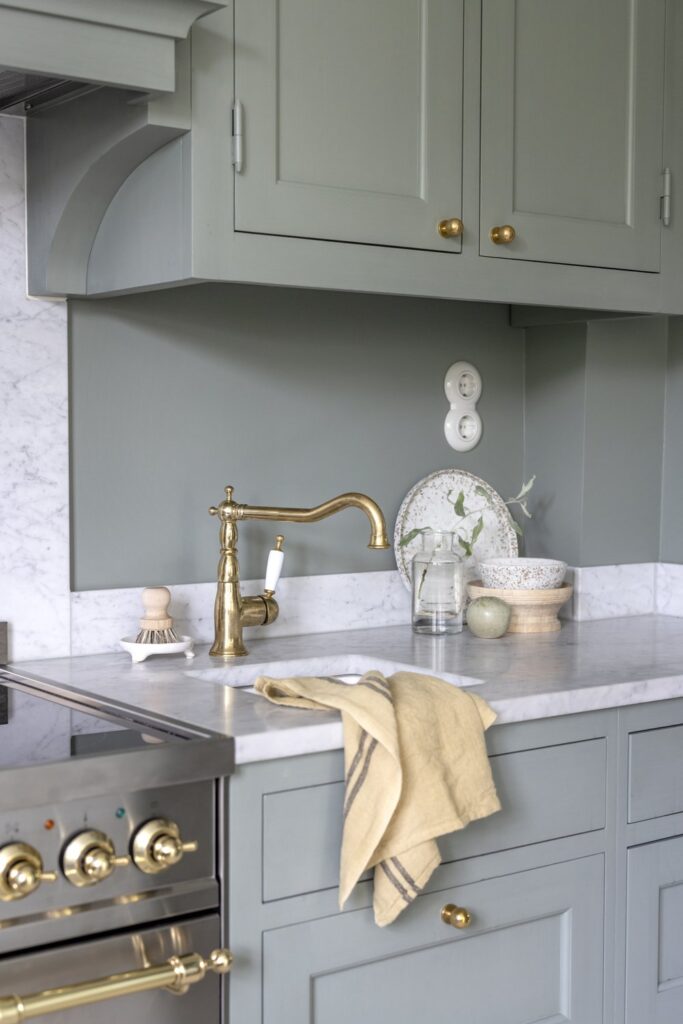 A green shaker kitchen with white marble countertops and gold details in the hardware