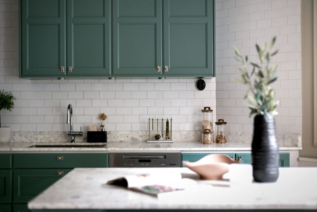 A green kitchen with a stone countertop, subway tiles and a kitchen isalnd
