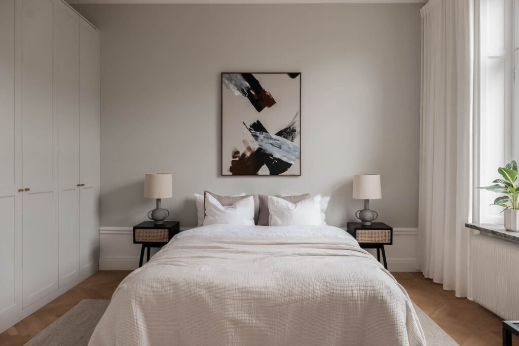 A modern bedroom with light grey walls, light grey wardrobe, black rattan side tables