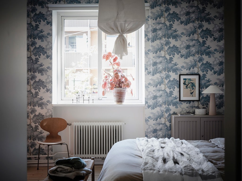 A blue pattern bedroom wallpaper in a romantic bedroom design with white and beige bedding