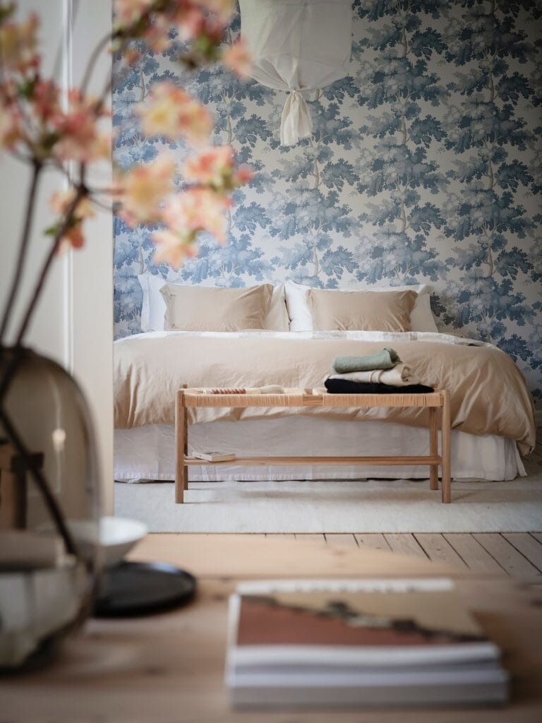 A blue pattern bedroom wallpaper in a romantic bedroom design with white and beige bedding
