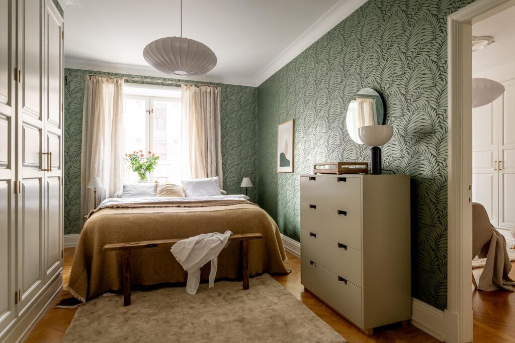A bedroom with a green botanical wallpaper design and a beige decor