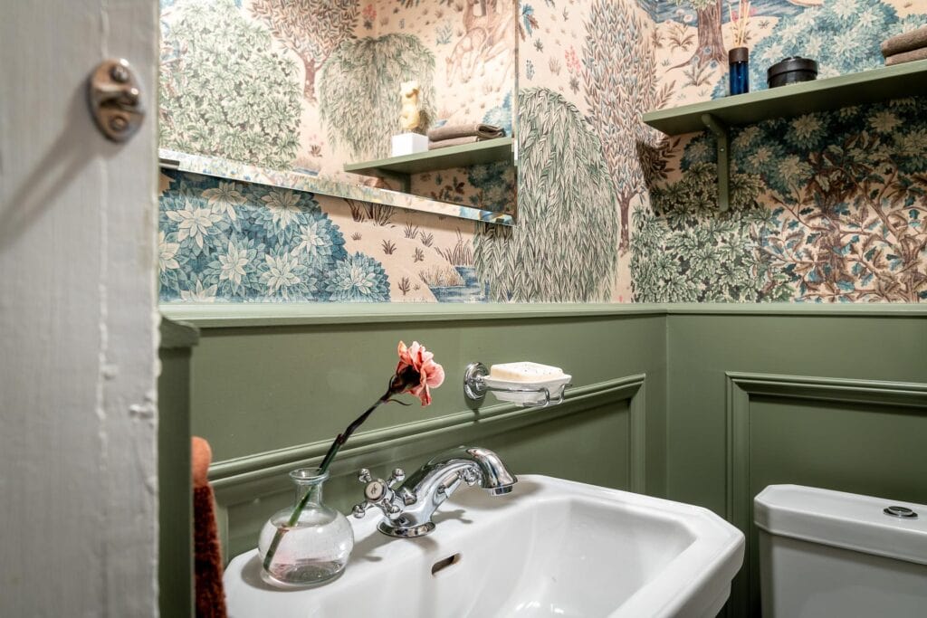 A guest bathroom with green wainscoting and a beautiful bathroom wallpaper