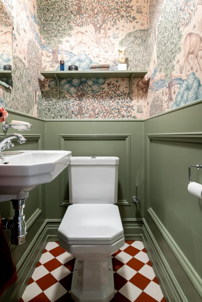 A guest bathroom with green wainscoting and a beautiful bathroom wallpaper