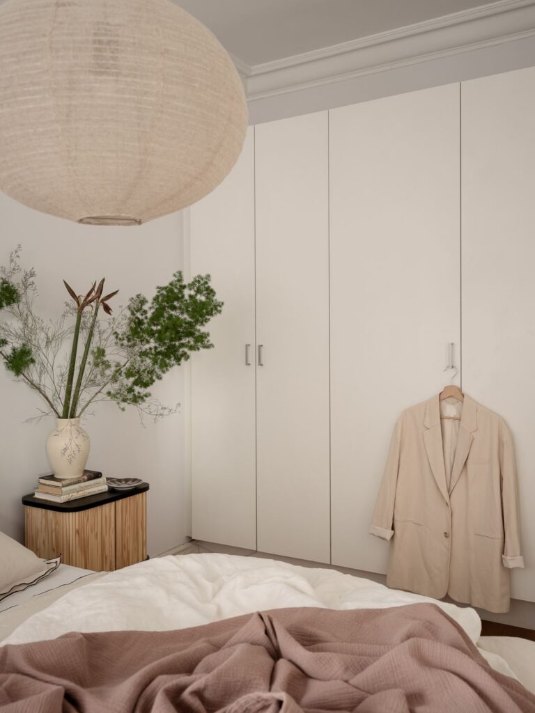 A bedroom with a natural color palette and a white wardrobe spread across the wall