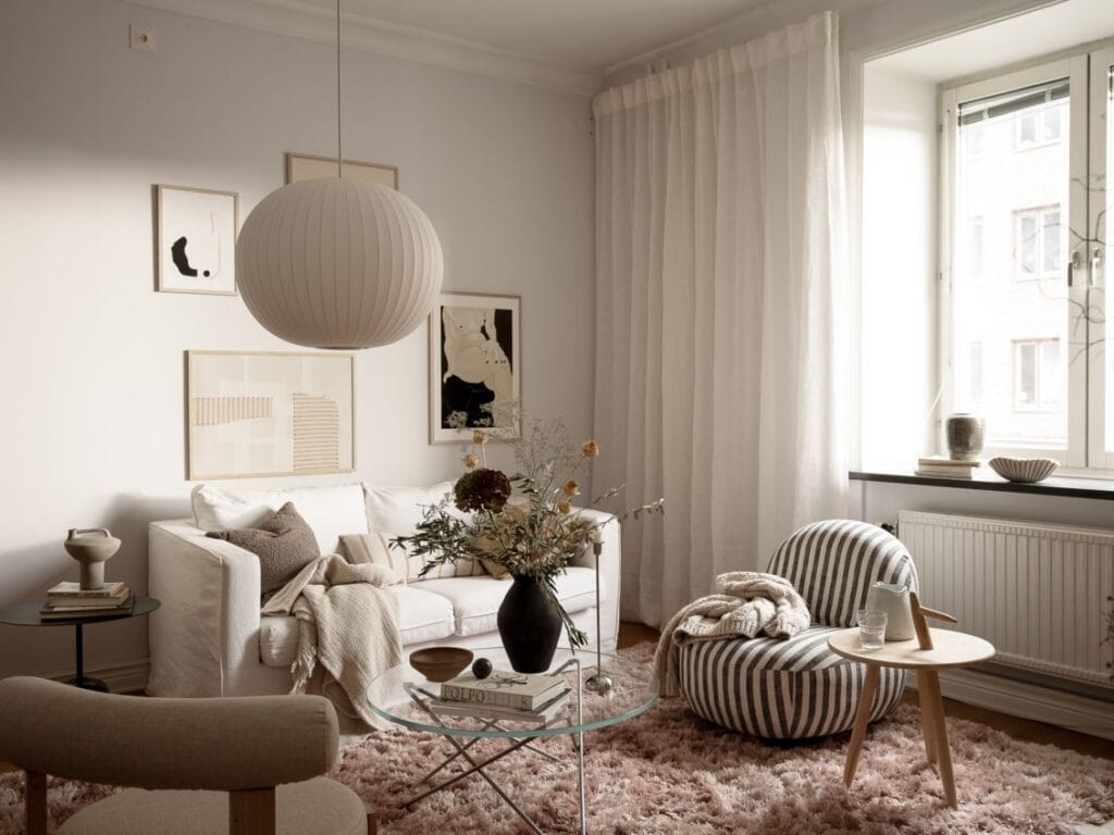 A living room with a white sofa and a gallery wall in beige and black tones, paired with a pink area rug and a striped lounge chair