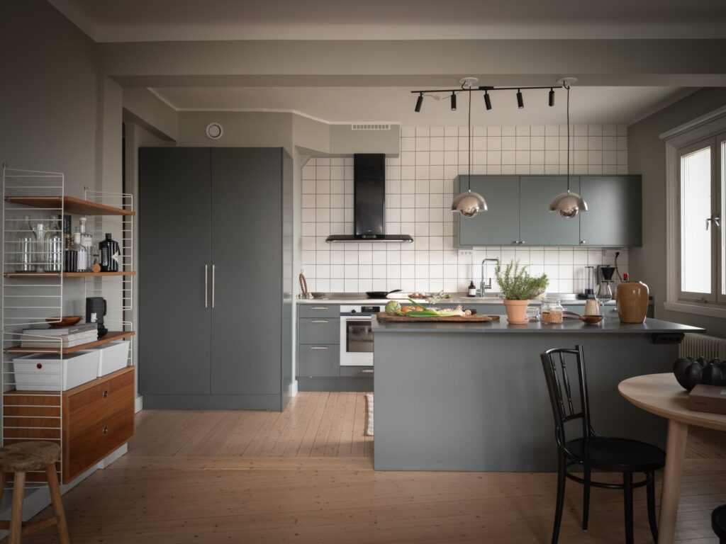 A dark green-grey kitchen with a stainless steel countertop and a white tile backsplash