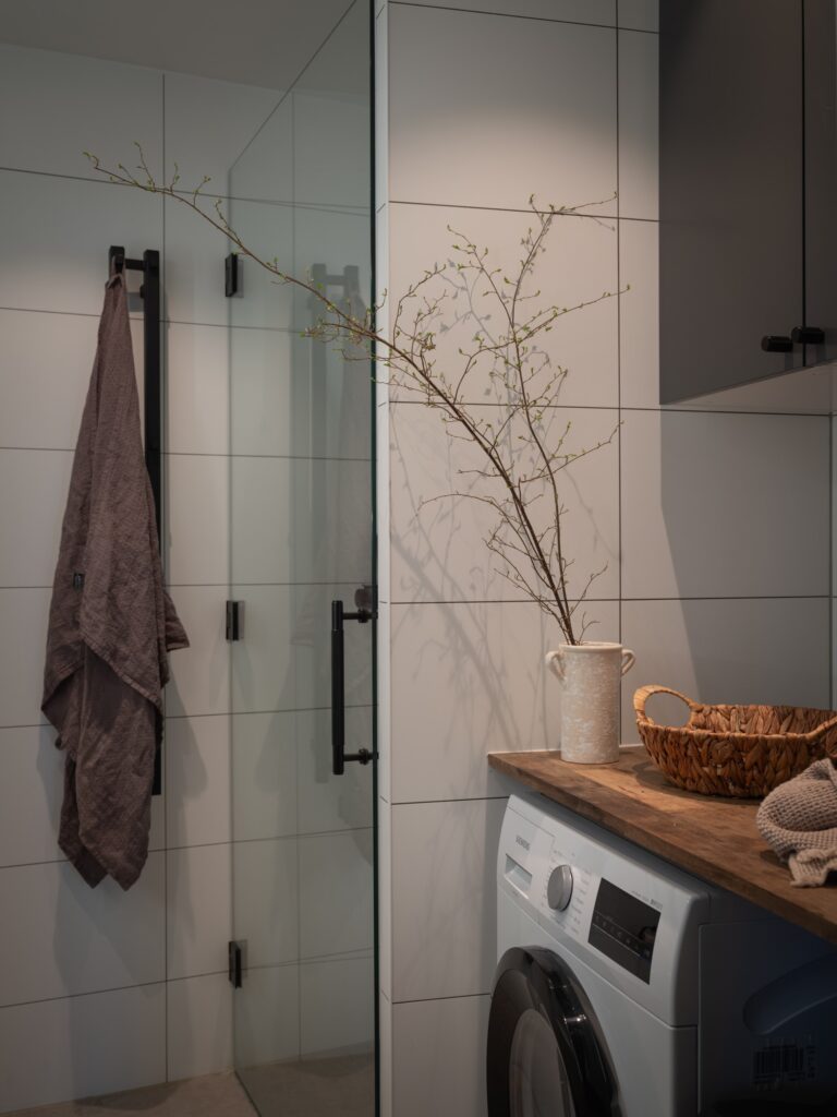A modern bathroom with white wall tiles, washing machine, and black fixtures