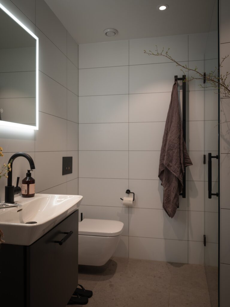 A modern bathroom with white wall tiles, beige floor tiles, and black fixtures