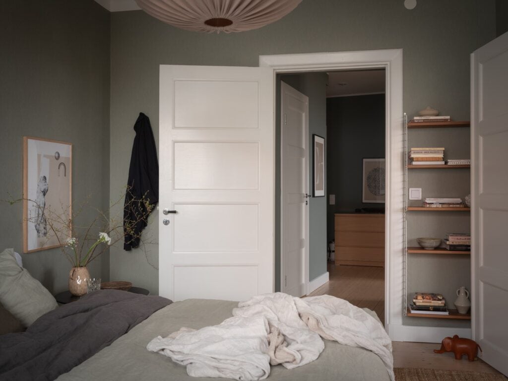 A master bedroom with a dark green-grey wall color and neutral decor