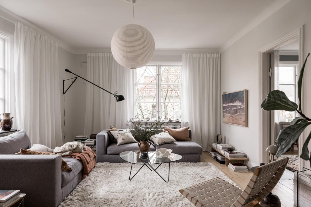 A living room with white walls, white curtains and a set of grey couches