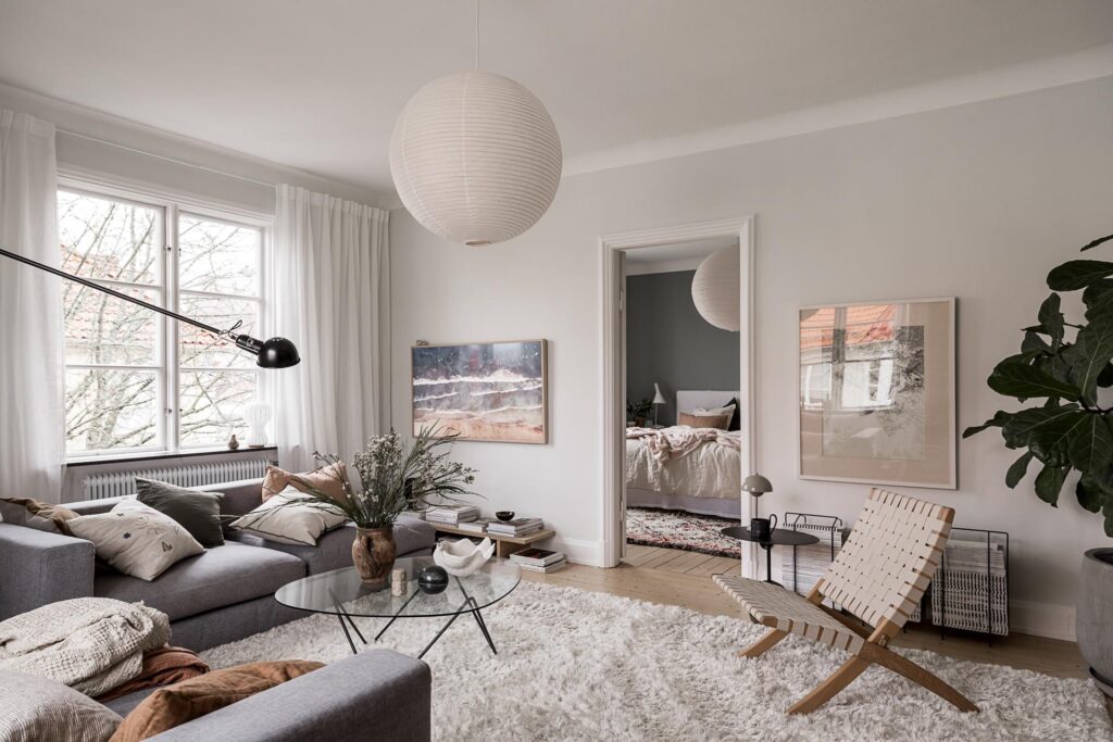 A living room with white walls, white curtains and a set of grey couches