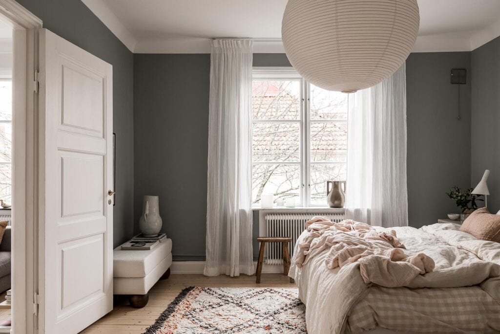 A bedroom with a dark grey wall color and white, beige and brown tones in the textiles