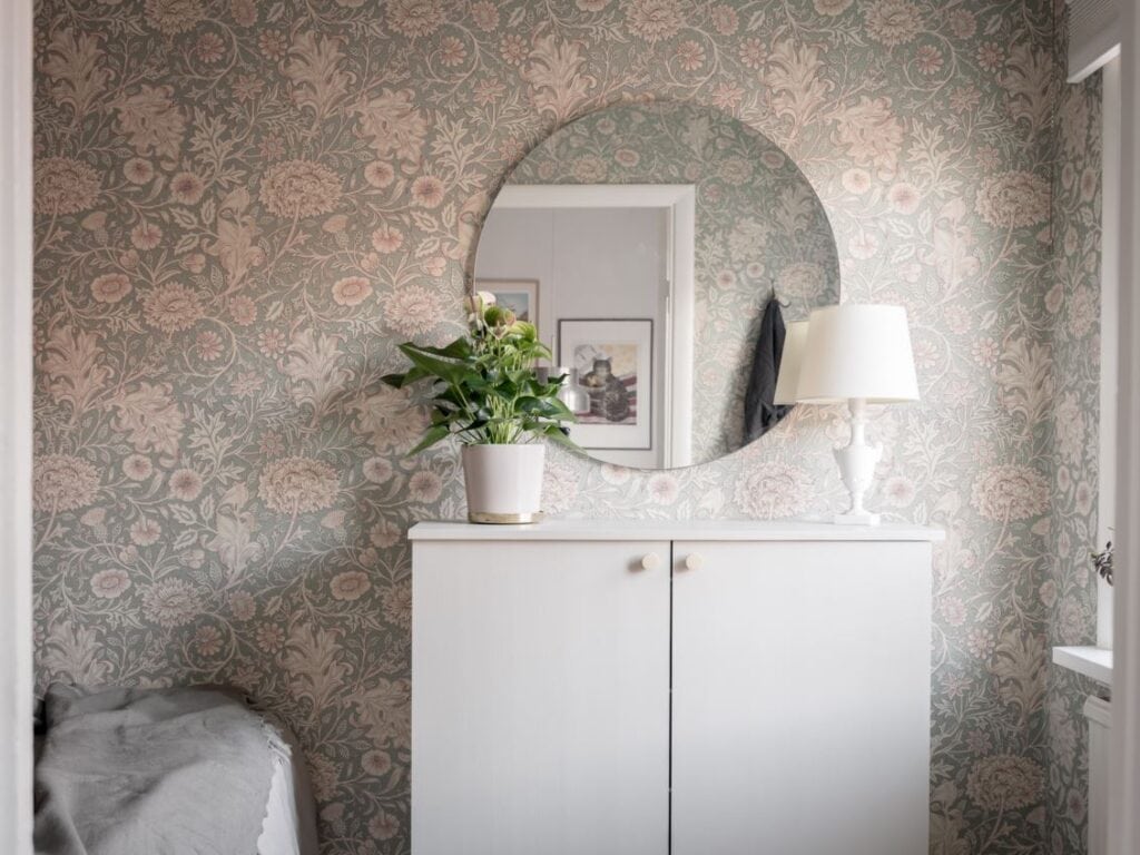 A bedroom with a sage green floral wallpaper