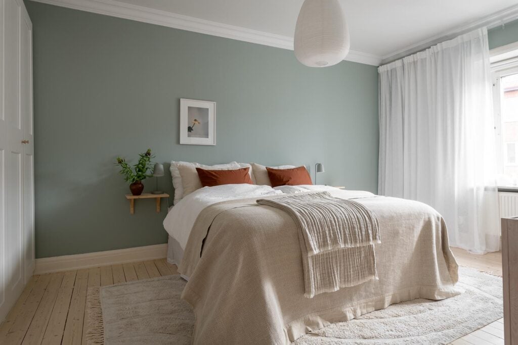 A sage green bedroom with a white wardrobe and terracotta accent pieces