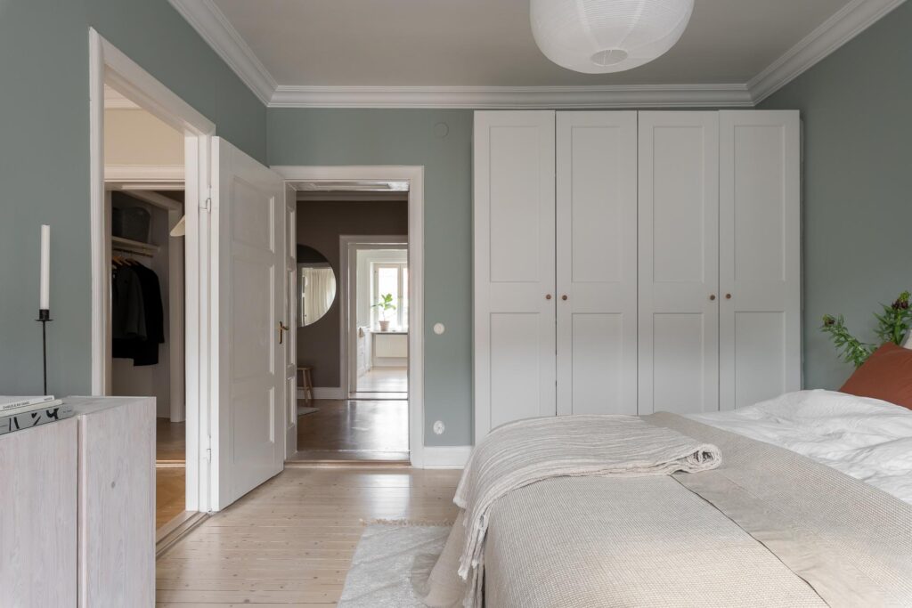 A sage green bedroom with a white wardrobe and terracotta accent pieces