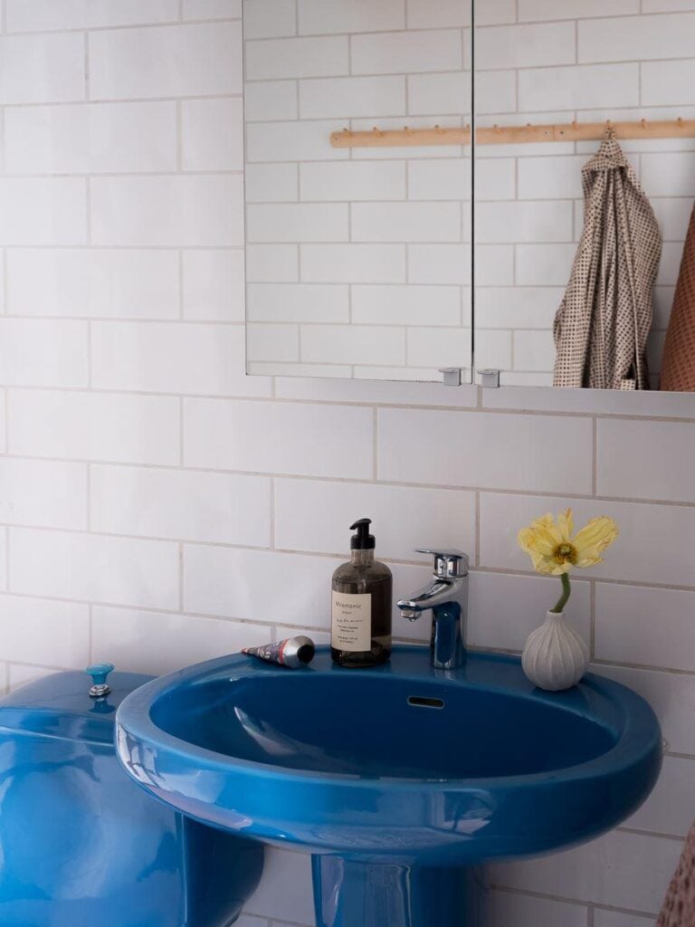 A bathroom with white subway tiles on the wall and a blue sink and toilet