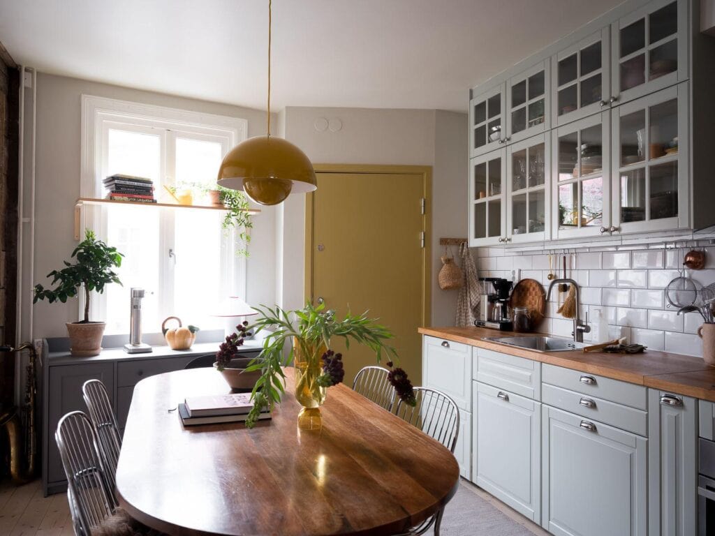 A mint green kitchen with butcher block countertops, a white subway tile backsplash and upper glass cabinets with a yellow pantry door