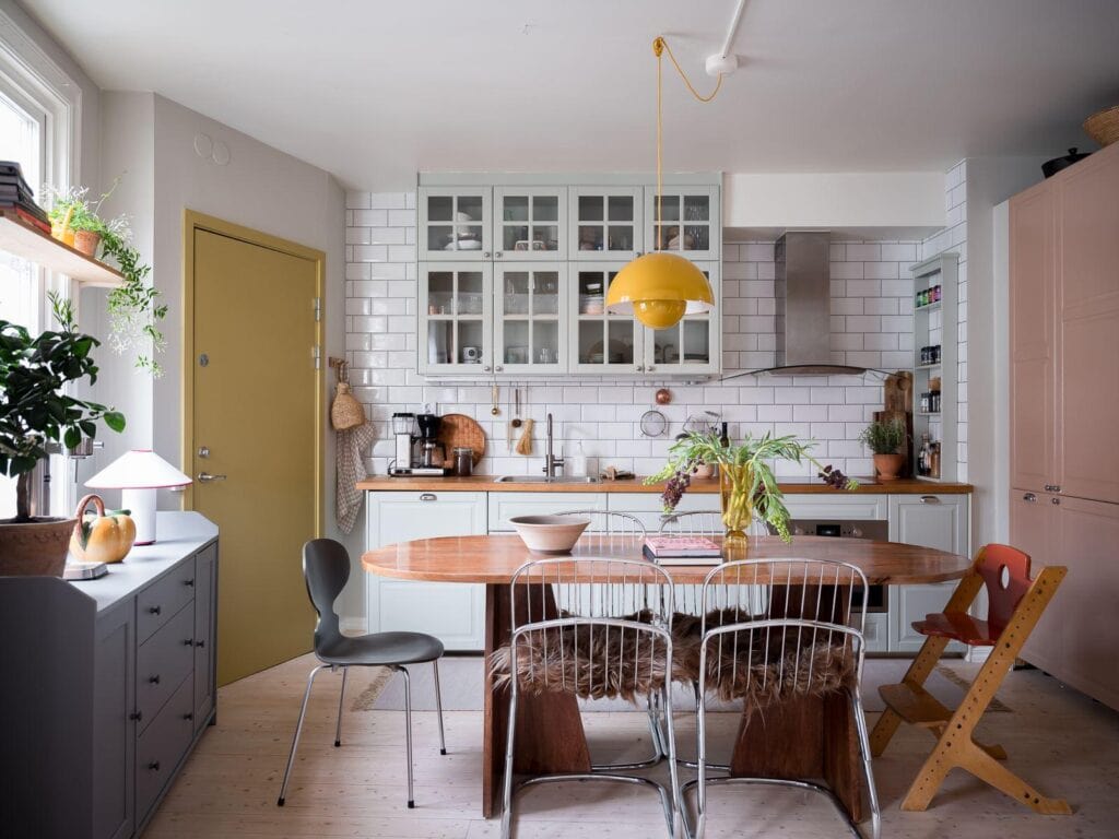 A mint green kitchen with butcher block countertops, a white subway tile backsplash and upper glass cabinets with a vintage dining table in the middle
