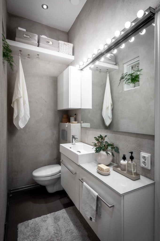 A bathroom with a concrete finish on the walls, white vanities
