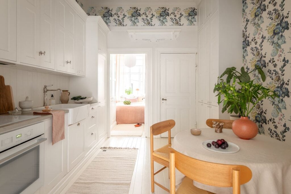 A white shaker kitchen with stainless steel hardware a tile and shiplap backsplash, floral wallpaper