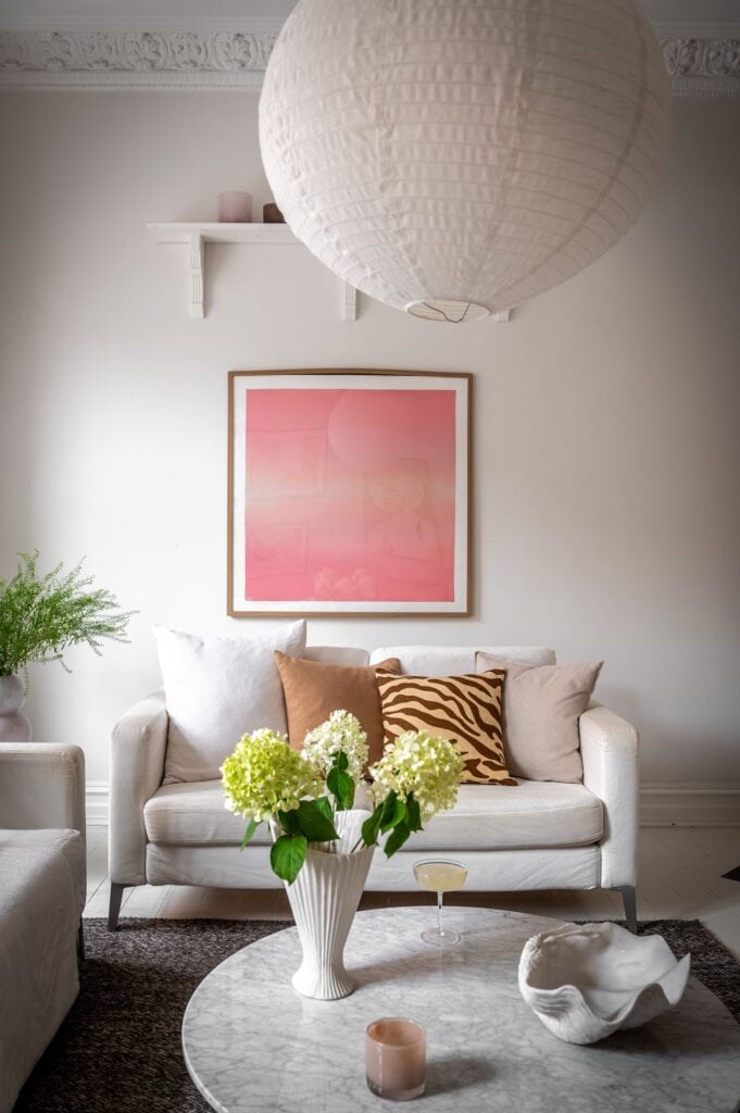 A living room with off-white walls, colorful art prints, grey rug, white sofas