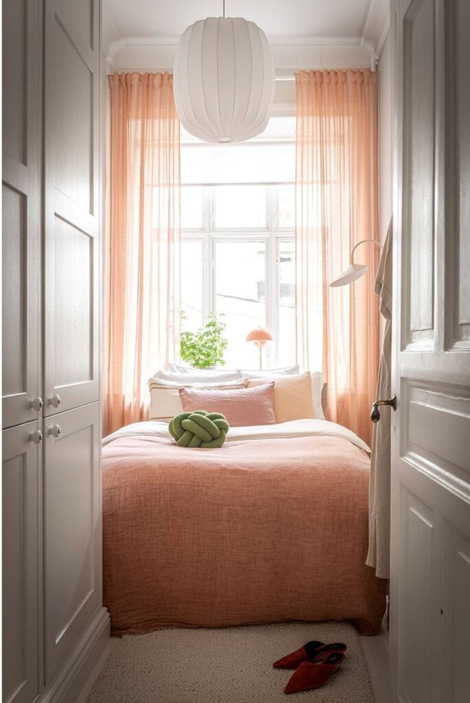 A small bedroom with pink curtains and pink bedding