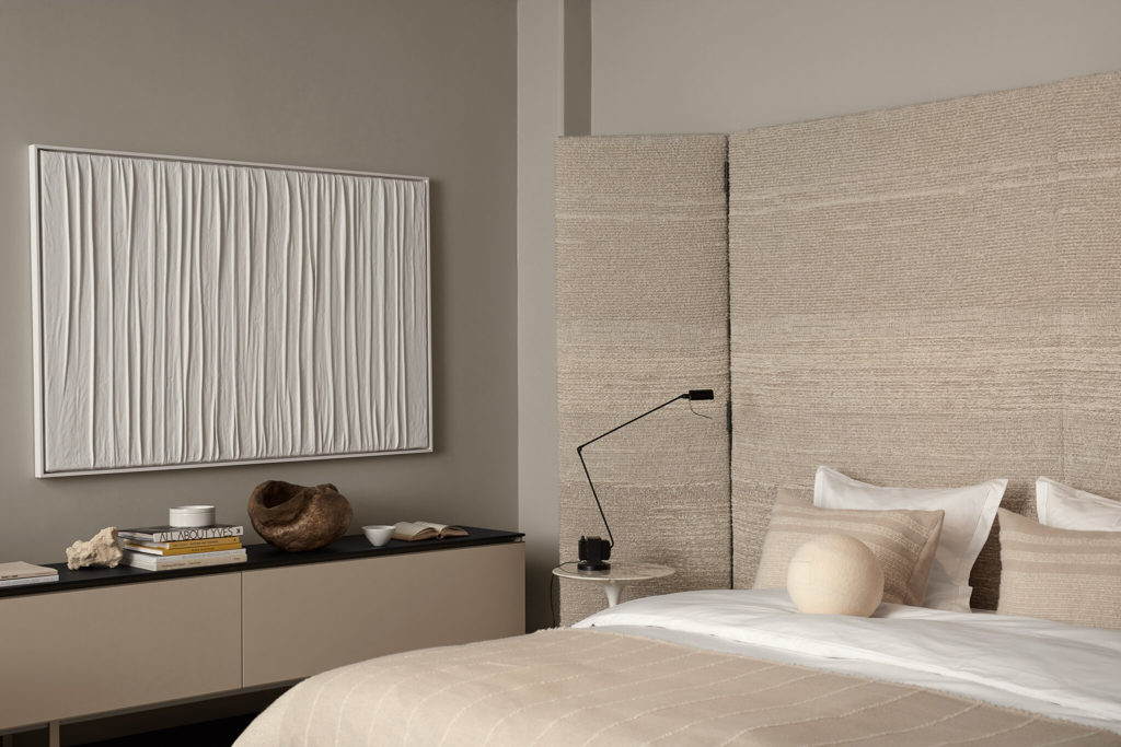 A bedroom with greige walls, beige fabric headboard, beige bedding, white headboard