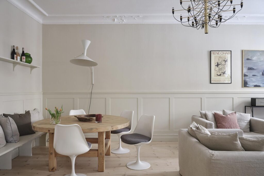 A dining area with wainscoting, a custom seating bench, wood table and white wall lamp