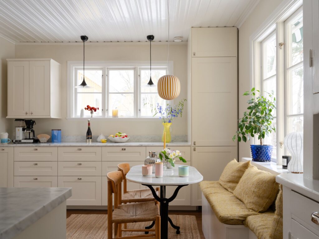 A white shaker kitchen with a window seat, decorates with pops of color