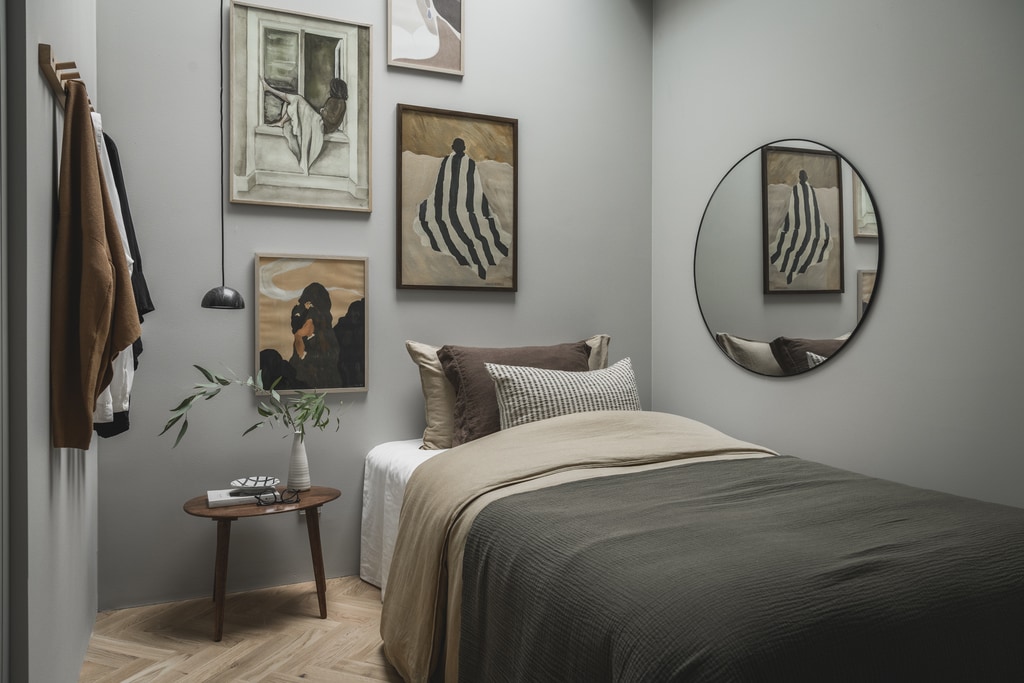 A small light grey bedroom with a gallery wall reflected in a round mirror