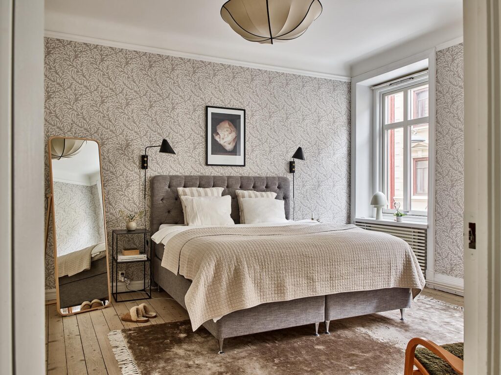 A beige pattern bedroom wallpaper paired up with wood, grey, beige and black tones in the furnishings