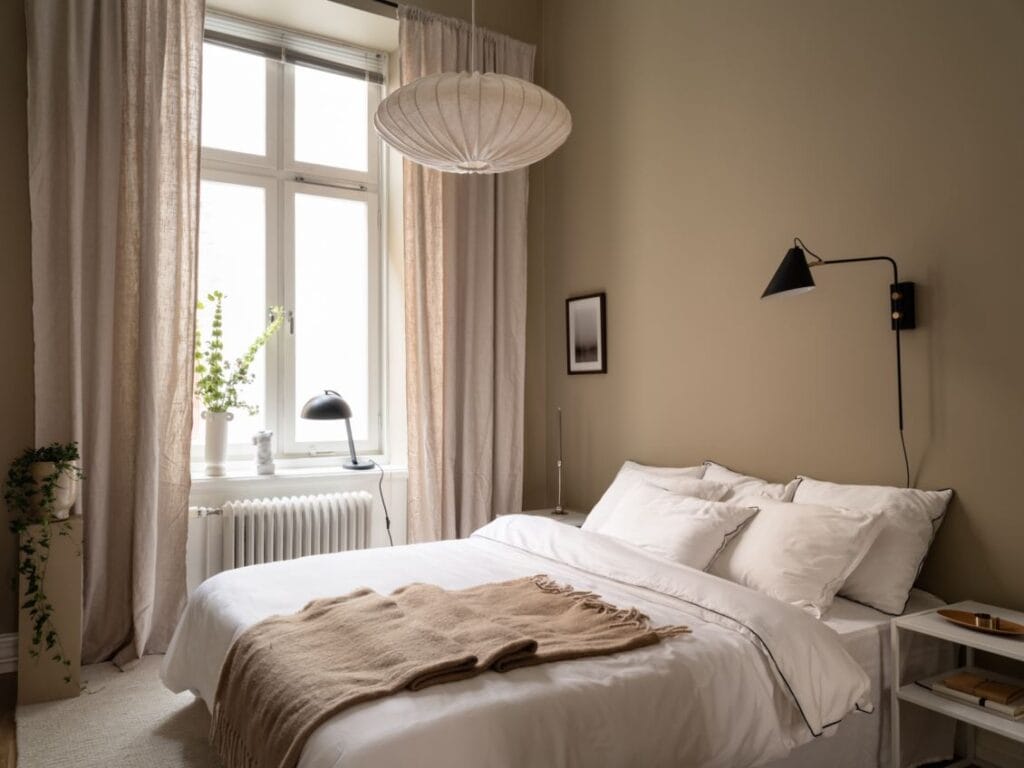 A minimal bedroom with beige walls, white bedding, beige curtains and black accent lamps